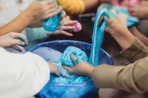 Kids around a table stretching slime with their hands that was created for a STEM activity.